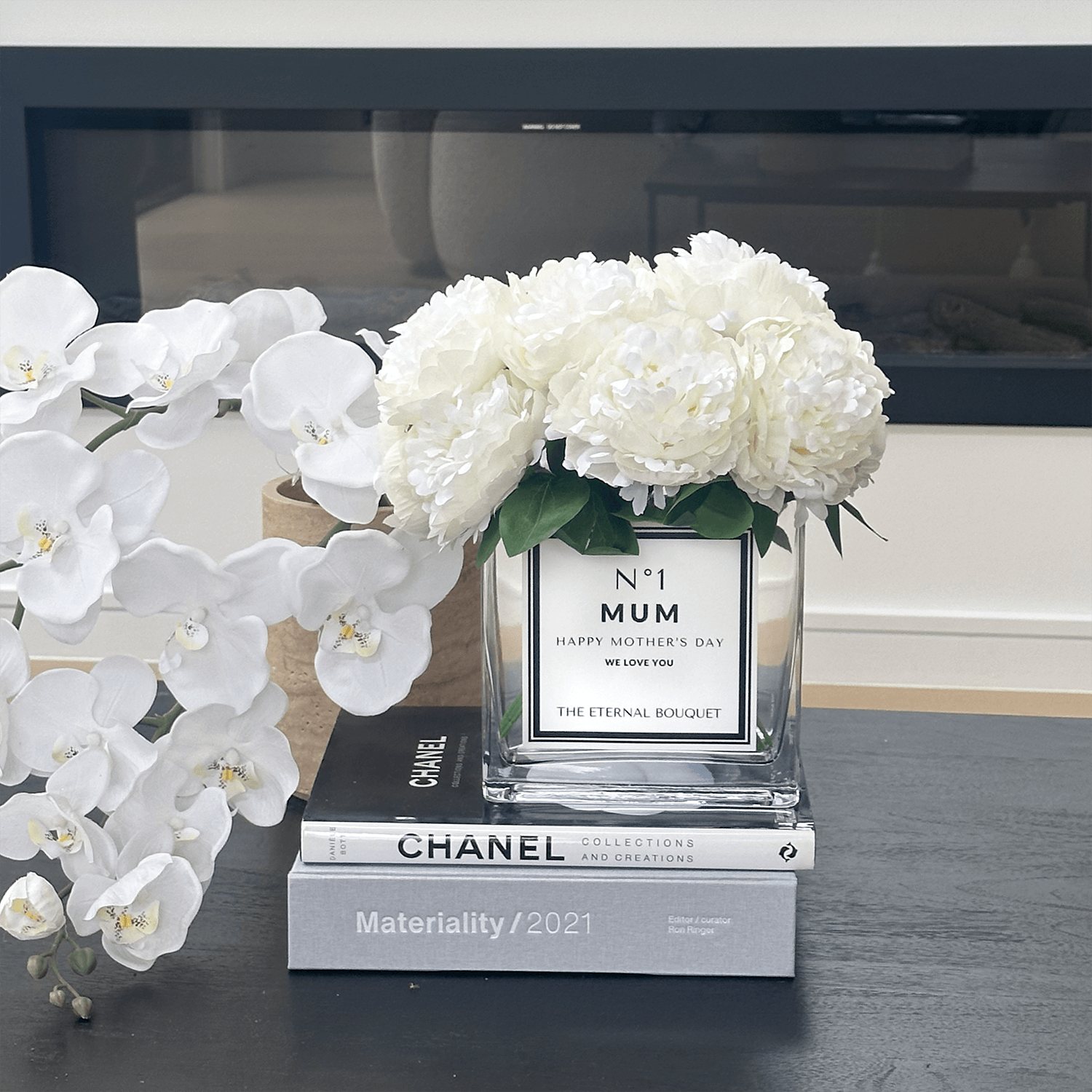 White peonies in glass vase with customised label in living room.