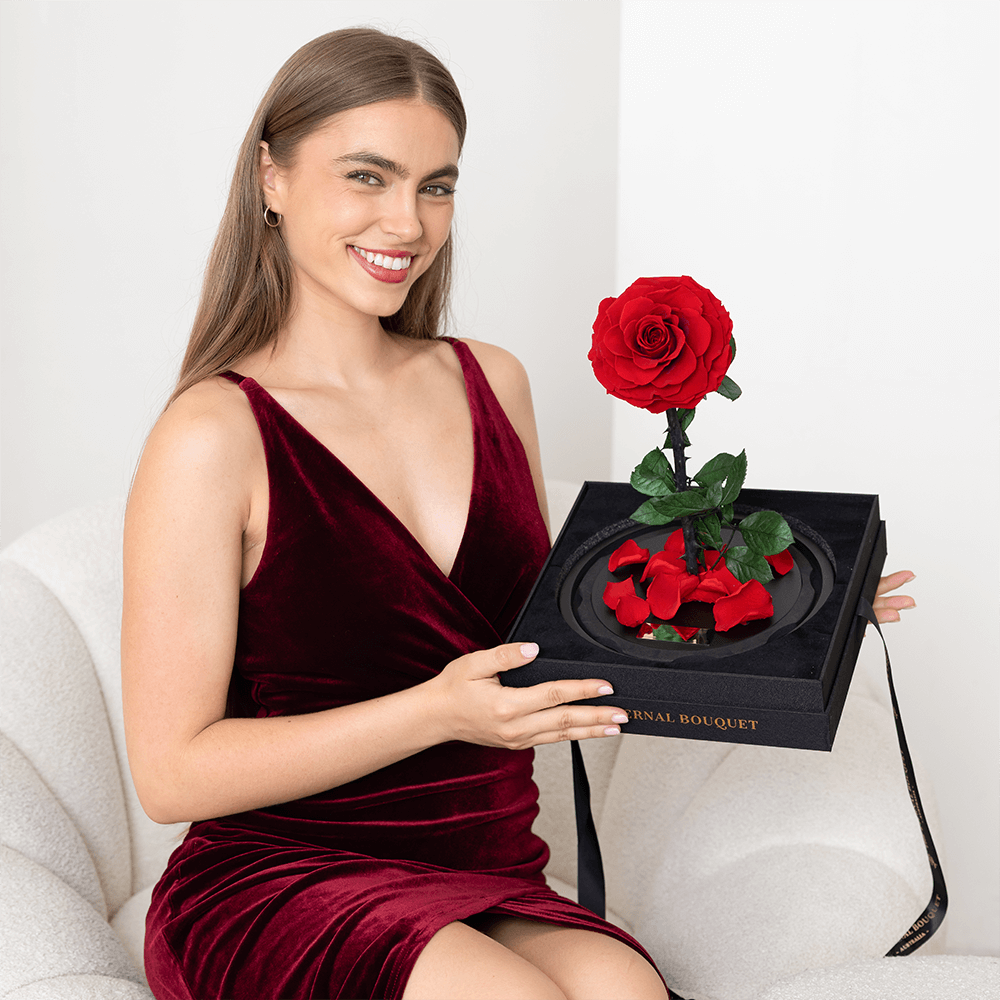 Woman holding a preserved red rose with scattered petals on black display base