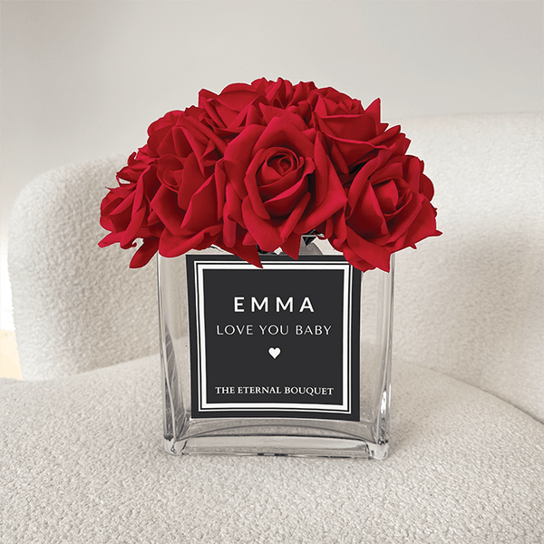 Personalised glass vase with scented red roses and a customised label.