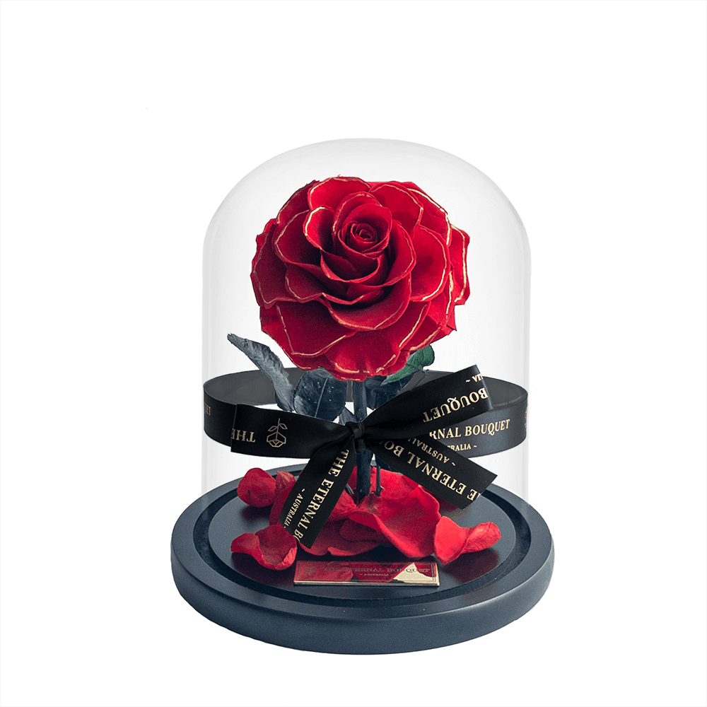 A mini everlasting red rose in full bloom, displayed under a crystal-clear glass dome and set on a sleek black base, elegantly tied with The Eternal Bouquet's signature black and gold ribbon. This timeless floral arrangement makes the perfect romantic gift, symbolising everlasting love while requiring no maintenance. Ideal for anniversaries, Valentine's Day, or meaningful milestones.