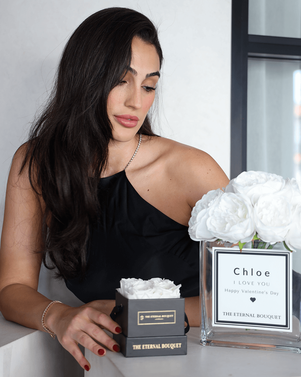 A luxurious arrangement of elegant white peonies from The Eternal Bouquet, beautifully displayed in a clear glass square vase. The vase features a minimalist white label with black borders, personalised, adding a chic, designer-inspired touch. This everlasting flower arrangement is perfect for sophisticated gifting, offering a timeless and elegant statement.