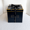 A sleek and elegant black gift box with gold accents and a luxurious black ribbon, featuring "THE ETERNAL BOUQUET" branding. The premium packaging sits on a soft, textured surface, exuding sophistication and exclusivity. This box is designed to hold the everlasting floral arrangements from The Eternal Bouquet, making it a perfect gift for any special occasion.