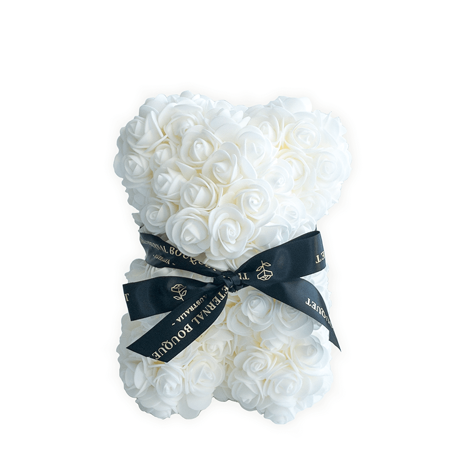 A luxurious everlasting white rose teddy bear from The Eternal Bouquet, crafted from delicate roses and tied with an elegant black and gold branded ribbon. This timeless piece makes a perfect gift for weddings, anniversaries, baby showers, or as a chic decorative item to brighten any modern space.
