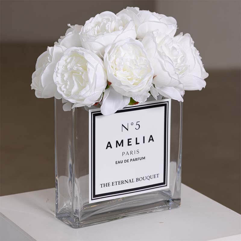 A luxurious arrangement of elegant white peonies from The Eternal Bouquet, beautifully displayed in a clear glass square vase. The vase features a minimalist white label with black borders, personalised, adding a chic, designer-inspired touch. This everlasting flower arrangement is perfect for sophisticated gifting, offering a timeless and elegant statement.