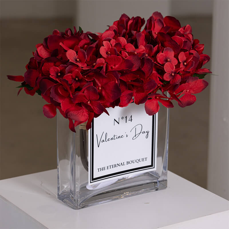 A luxurious everlasting flower arrangement from The Eternal Bouquet, featuring deep red hydrangea blooms in a clear personalised glass vase labelled 'No. 14 Valentine's Day'. The elegant design makes it a perfect romantic gift or decorative piece for Valentine's Day.