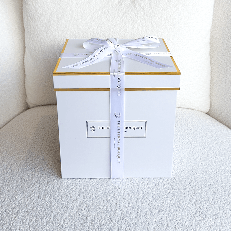 A luxurious white gift box with gold accents and a neatly tied white ribbon, featuring 