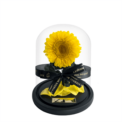 A stunning everlasting sunflower encased in a sleek glass dome, tied with an elegant black ribbon featuring 'The Eternal Bouquet' in gold lettering. Resting on a sophisticated black base, this timeless arrangement captures the warmth and joy of sunflowers, symbolizing happiness and positivity. A perfect gift for brightening someone’s day, celebrating special moments, or adding a cheerful touch to any space. 