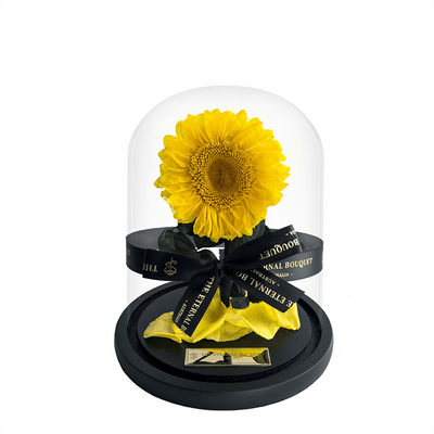 A stunning everlasting sunflower encased in a sleek glass dome, tied with an elegant black ribbon featuring 'The Eternal Bouquet' in gold lettering. Resting on a sophisticated black base, this timeless arrangement captures the warmth and joy of sunflowers, symbolizing happiness and positivity. A perfect gift for brightening someone’s day, celebrating special moments, or adding a cheerful touch to any space. 