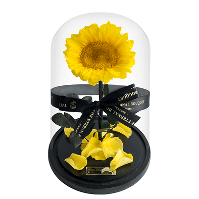 An everlasting sunflower elegantly encased in a glass dome and tied with a signature black ribbon from The Eternal Bouquet. Resting on a sleek black base with scattered yellow petals, this radiant piece brings warmth and cheer to any space, making it a thoughtful gift for birthdays, get-well wishes, or to brighten someone's day with a lasting symbol of joy and positivity.